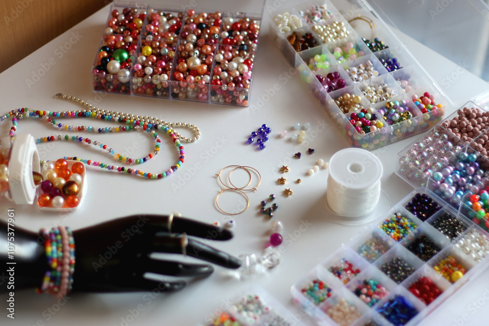 Obraz premium Hand figurine, colorful friendship bracelets, necklaces, various beads and DIY supplies on the table. Making jewelry at home. Selective focus.