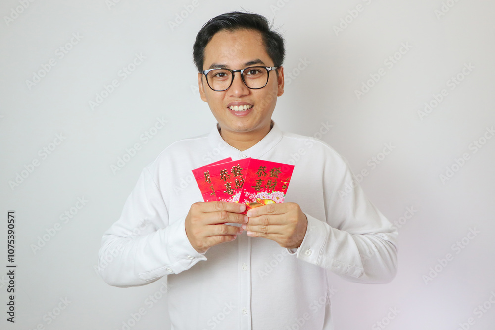 Happy Chinese new year. Asian man holding angpao or red packet monetary gift isolated on red decoration background. Chinese text means great luck great happy. Happy Chinese new year. Asian man holding angpao or red packet monetary gift isolated on red decoration background. Chinese text means great luck great happy.