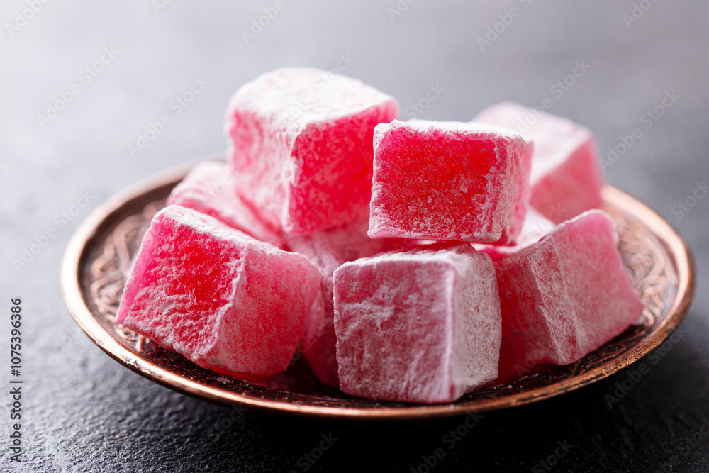 Turkish delight, rose flavour in a copper plate. Grey background. Close up. Turkish delight, rose flavour in a copper plate. Grey background. Close up.