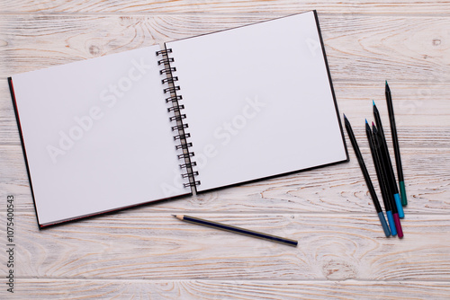 Top View of Open Sketchbook with Colored Pencils on Wooden Background