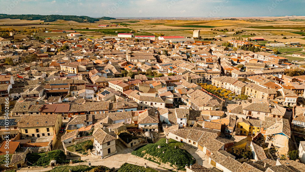 Obraz premium Panoramic view of the historic town of Astudillo, Spain, showcasing the medieval La Mota Castle and traditional hillside wineries. Captures rural charm and architectural heritage.