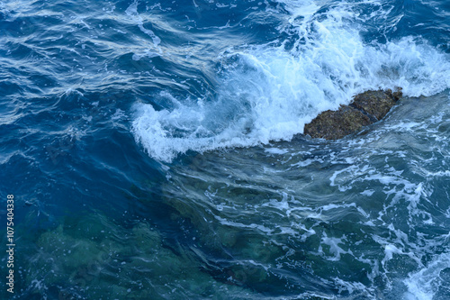 Waves crash against a rocky shoreline during a vibrant sunny day at the coast.