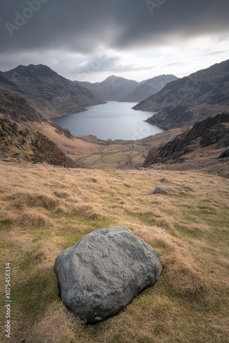 a large rock sits on the grass in front of a lake photo