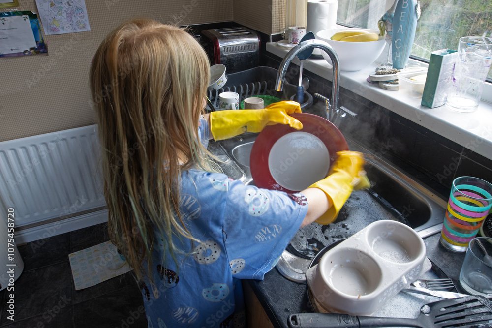 Child (8-9 years old) in Yellow marigold gloves washing up inside kitchen during day washing plate