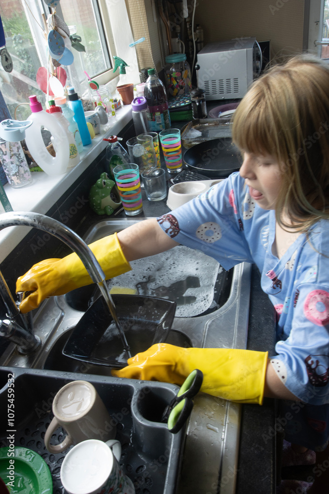 Child (8-9 years old) in Yellow marigold gloves washing up inside kitchen during day washing plate