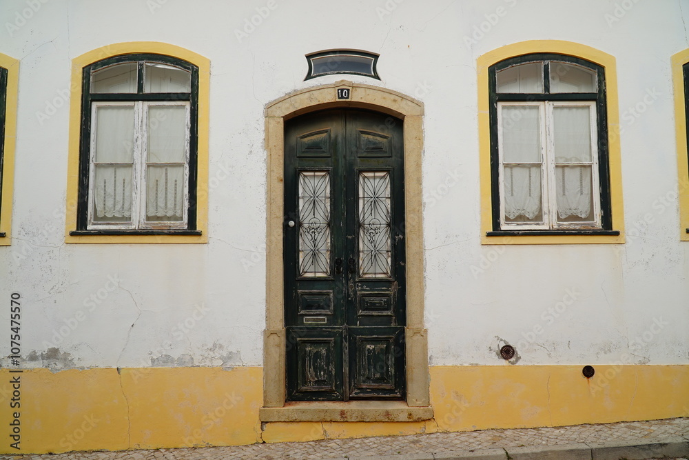Fototapeta premium Wooden weathered old front door with mailbox with the Portuguese inscription for mail (correio), detail of a yellow and white house facade in the village of Vila do Bispo, Algarve, Portugal.