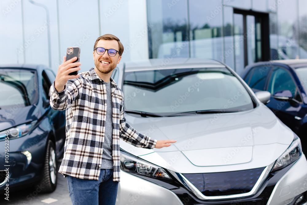 Happy man taking selfie through smart phone after purchasing new car. The man showing the purchased car via video link over the phone Happy man taking selfie through smart phone after purchasing new car. The man showing the purchased car via video link over the phone