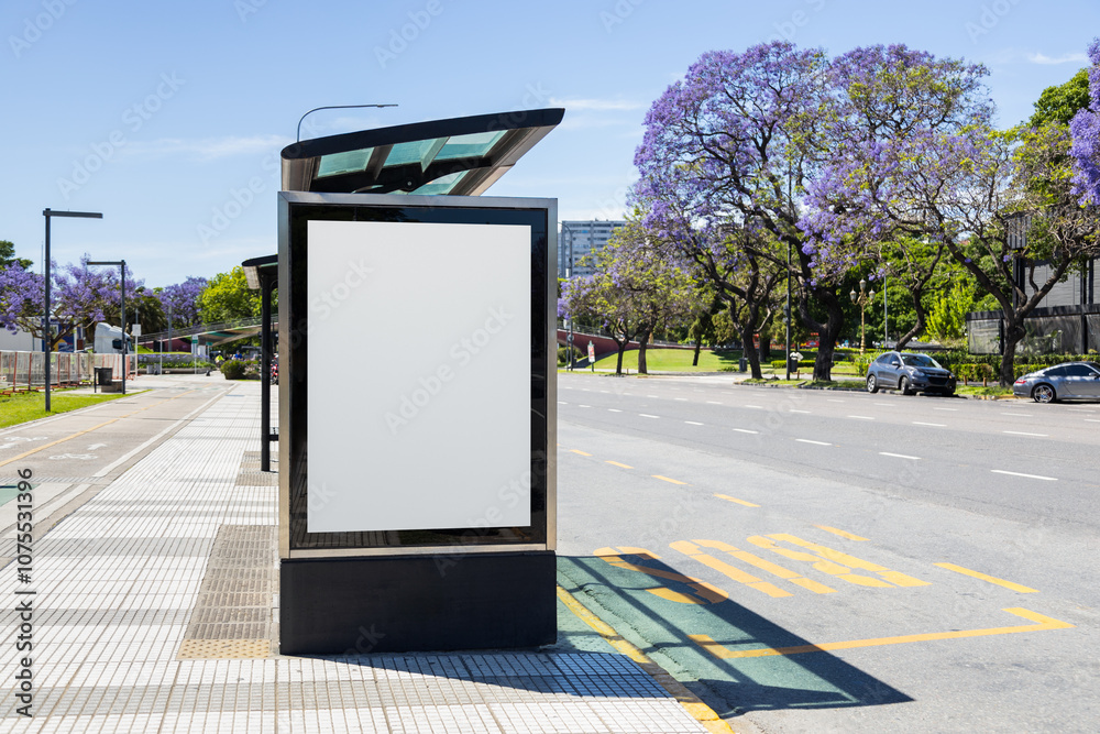 Vertical blank billboard at a bus stop shelter in Buenos Aires, Argentina with jacaranda trees blooming along Libertador avenue in spring. Copy space poster on a lightbox for displaying ad content