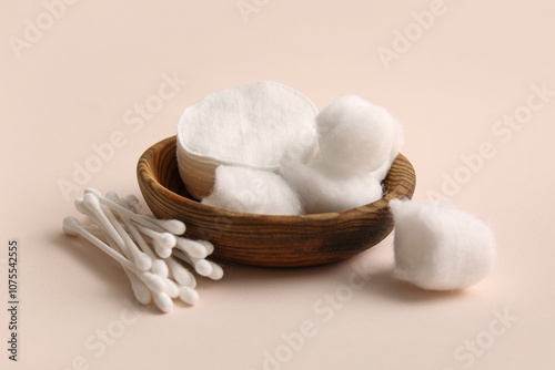 Wooden bowl with cotton balls, pads and swabs on beige background photo