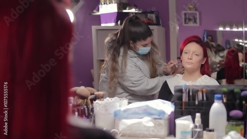 Makeup Artist Applying Character Makeup to Redhead Woman – Mid Shot Reflected in Mirror. Maquilladora Aplicando Maquillaje de Caracterización a Mujer Pelirroja – Plano Medio Reflejado en el Espejo
