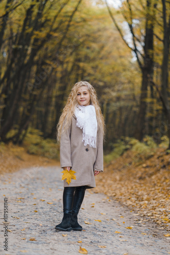 A beautiful girl with fair hair in a coat walks through the autumn forest