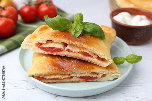 Pieces of tasty vegetarian calzone with tomato, cheese and basil on white textured table, closeup