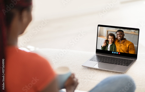 A mother enjoys a video call with her smiling child, creating a moment of connection and joy. The warm light from the afternoon sun brightens their cozy living space.