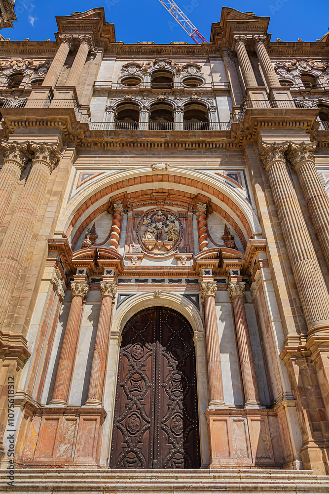 Obraz premium Fragments of majestic facade of Malaga Cathedral (1782), Baroque and Renaissance architecture with grand columns, detailed carvings, and archways under a clear blue sky. Malaga, Andalusia, Spain.