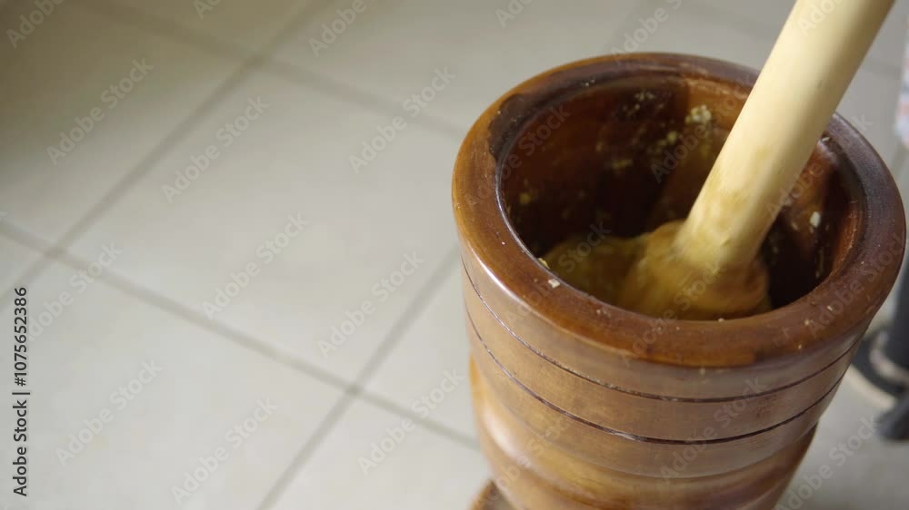 Close up at the hands of a person using a traditional wooden mortar, kneading bananas and mixing with spices Close up at the hands of a person using a traditional wooden mortar, kneading bananas and mixing with spices
