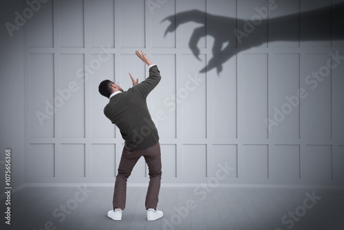 Man scared by monstrous hand reaching for him. Creepy shadow on light wall photo