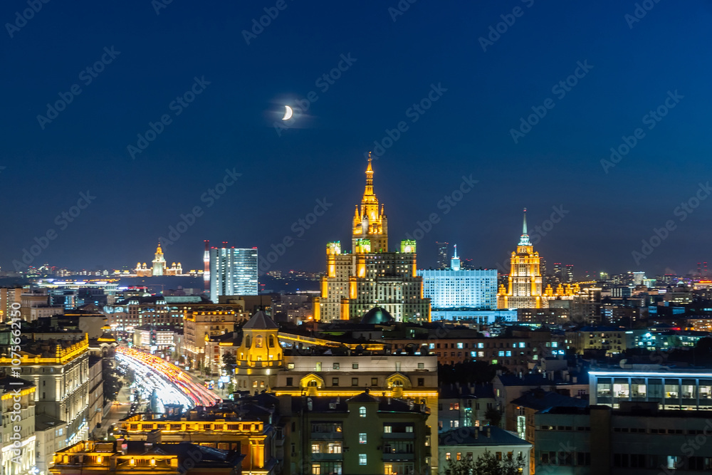 Obraz premium The skyline of Moscow sparkles with vibrant lights from historical buildings under a crescent moon, showcasing the city's beauty at night.