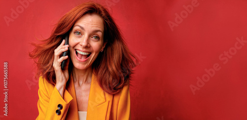 Photo of happy female leader with ginger hair, wears glasses, updates app on modern cell phone, wears stylish clothes