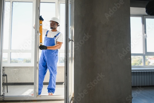 Young African Repairman In Overalls Installing Window