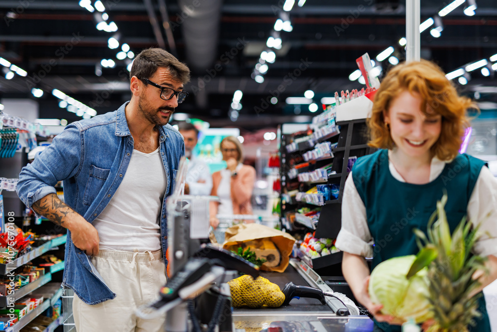 Fototapeta premium Customer watching cashier scanning groceries at supermarket checkout