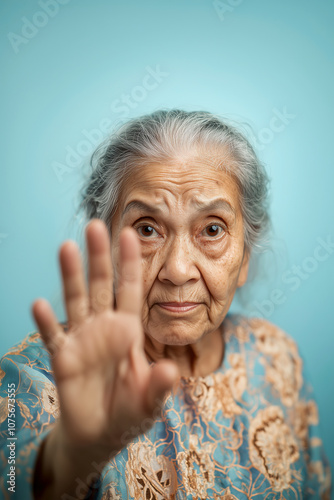 Elderly woman raising her hand, symbolizing a call to stop elder abuse and advocate for the rights and protection of seniors. Light blue background. photo