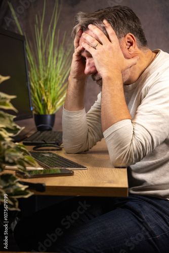 Wallpaper Mural un homme de 50 ans est en télétravail chez lui dans son bureau devant son ordinateur. Il travaille beaucoup et il est fatigué. Il se prend la tête dans les mains.	 Torontodigital.ca