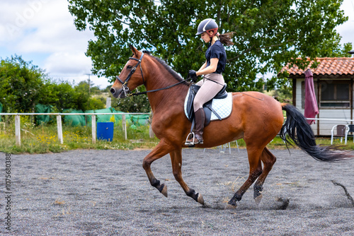 Woman riding a brown horse at a canter in an outdoor arena photo