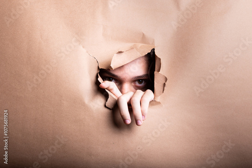 Man looking through a paper hole with his hands pushing the paper aside.