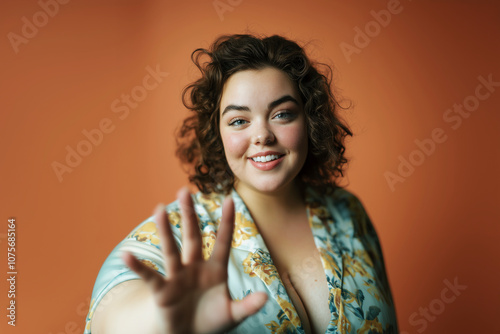 Smiling woman confidently extends her hand forward, addressing societal discrimination and challenges she faces with clothing due to her body size, advocating for body positivity and self-acceptance.  photo