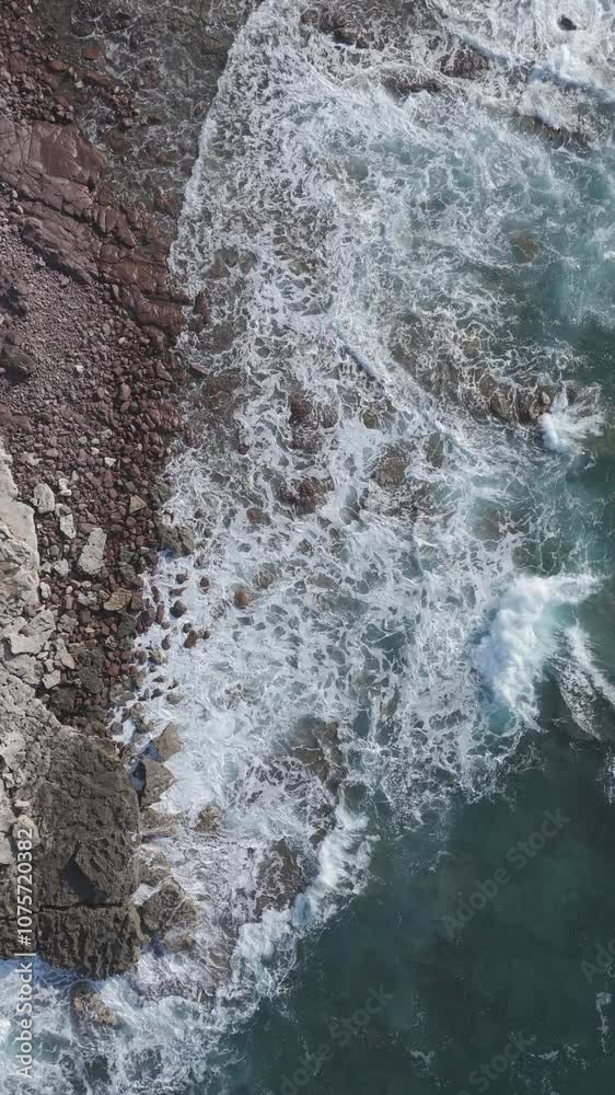 ripresa aerea in formato social verticale di delle onde forti che si infrangono sulla costa rocciosa. 