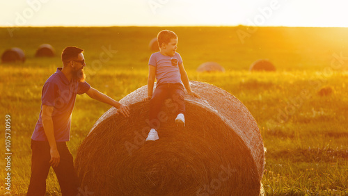 A father and his son sitting on a large hay bale in the haze of golden evening light photo