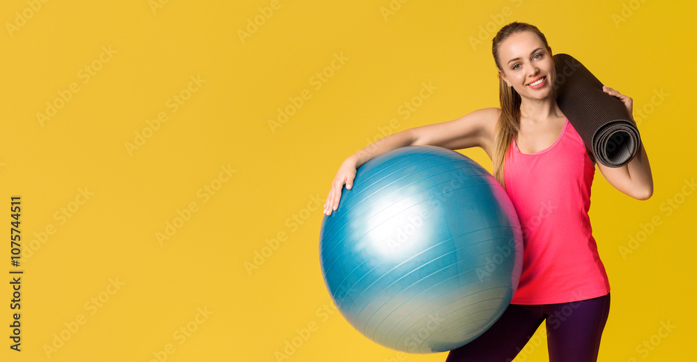 Fitness Concept. Portrait Of Young Sporty Woman With Fitball And Yoga Mat In Hands Standing Posing Over Yellow Background With Free Space Fitness Concept. Portrait Of Young Sporty Woman With Fitball And Yoga Mat In Hands Standing Posing Over Yellow Background With Free Space