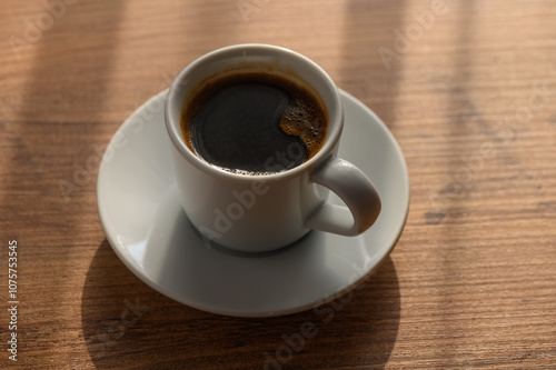 A steaming cup of coffee on a wooden table with morning light streaming in