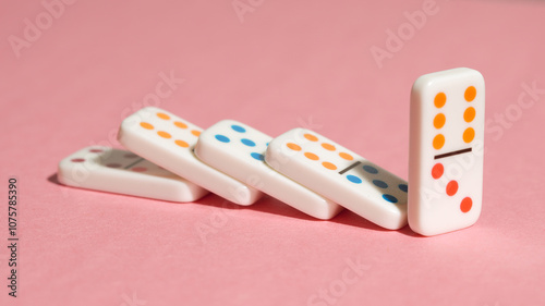 Fotografie Domino tiles falling in a row on a pink background, illustrating the domino effect