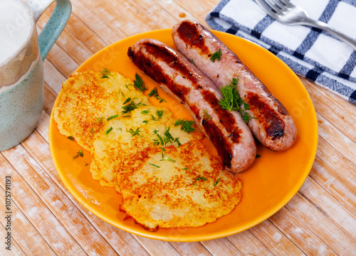 National dish of Belarusian cuisine is draniki, made from grated potatoes, served on a plate with fried sausages and ..decorated with herbs on top photo