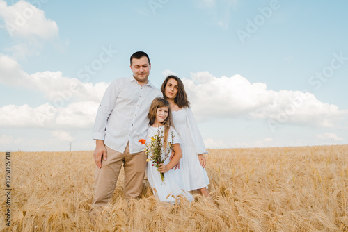 Happy family on a summer walk, mother, father and child walk in the wheat field and enjoy the beautiful nature, at sunset.Farmer family with little daughter walking through wheat field.