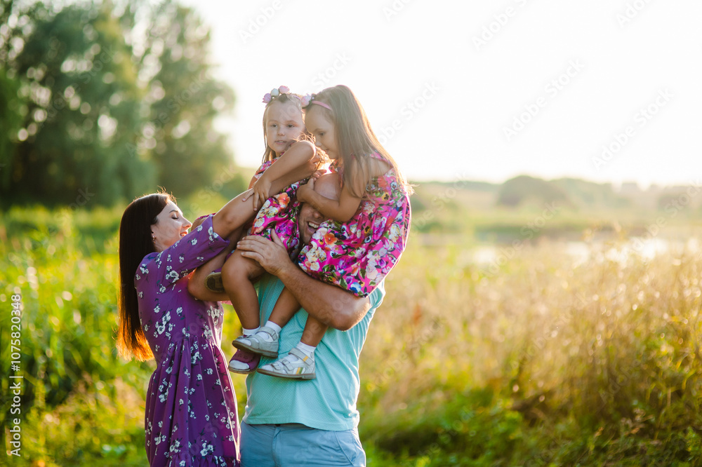 Fototapeta premium Children are having fun playing.Happy cheerful family in nature, weekend. Dad, mom and three children all in clothes, having a good time.Happy smiling family sitting on the grass in the park and look