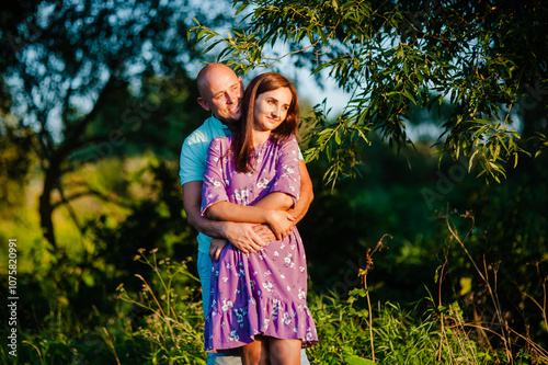 A happy mid-adult couple is tenderly hugging outdoors in a green park.The man and woman are smiling cheerfully while looking directly at the camera.
