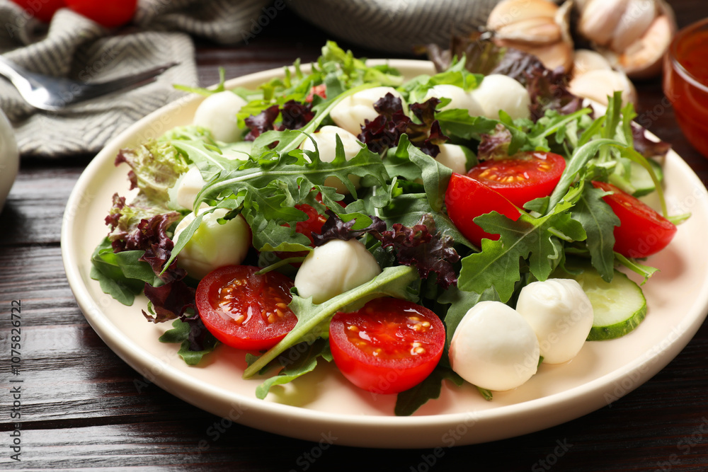 Tasty salad with arugula, lettuce, mozzarella cheese and vegetables on wooden table, closeup Tasty salad with arugula, lettuce, mozzarella cheese and vegetables on wooden table, closeup