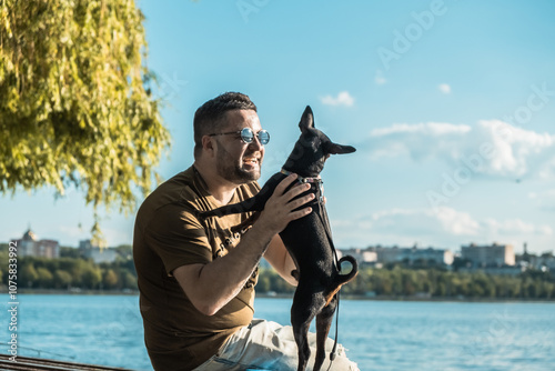 The black dog stands on its hind legs.Man sitting in the park and hugging and kissing his beautiful dog.