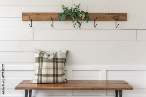 A rustic wooden wall hook shelf with greenery and a patterned cushion sits on a simple wooden bench against a white paneled wall. photo