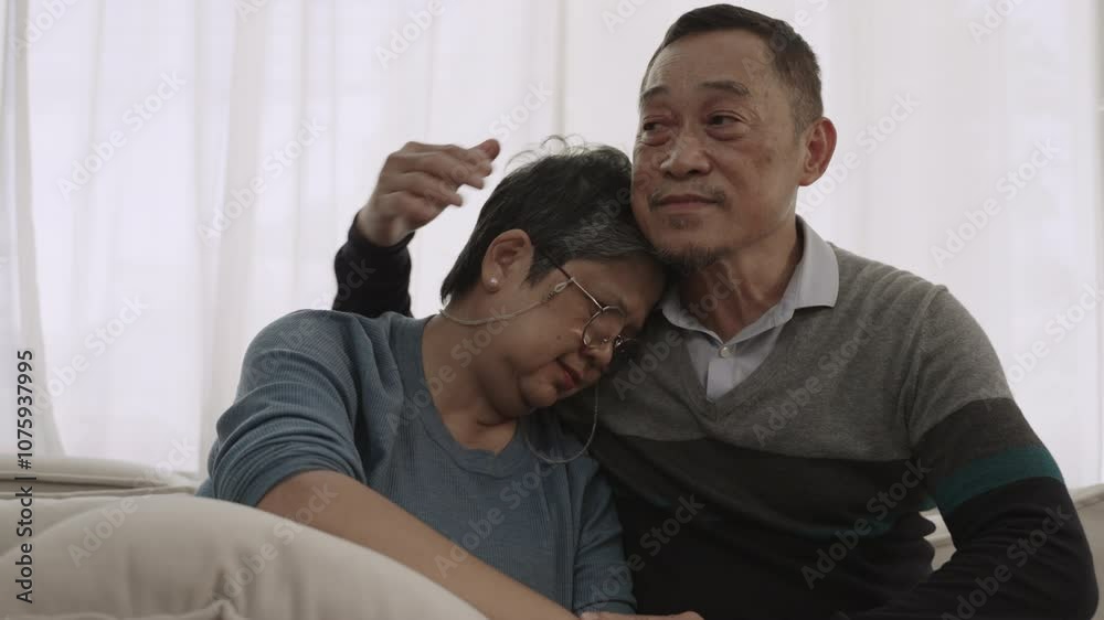 Unhappy senior Asian couple sitting embracing and consulting with supporting encourage each other on sofa in the living room at home. Mature husband sitting hugging and comforting his wife on couch. Unhappy senior Asian couple sitting embracing and consulting with supporting encourage each other on sofa in the living room at home. Mature husband sitting hugging and comforting his wife on couch.