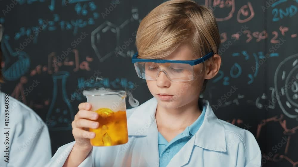 Closeup of smart boy inspect mixed chemical liquid in laboratory beakers while holding and looking carefully. Child focus on doing an experiment in chemistry lesson or STEM science class. Erudition. Closeup of smart boy inspect mixed chemical liquid in laboratory beakers while holding and looking carefully. Child focus on doing an experiment in chemistry lesson or STEM science class. Erudition.
