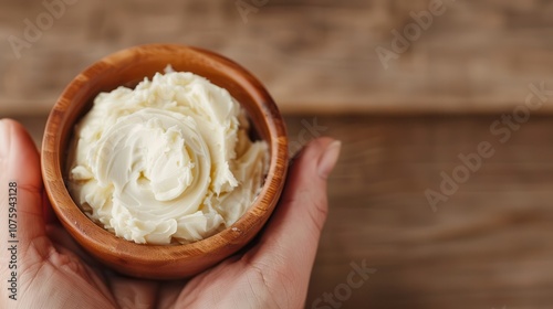 Palm oil shea butter. A creamy spread is served in a wooden bowl, held in a hand, against a rustic wooden background, ideal for culinary use or as a topping.