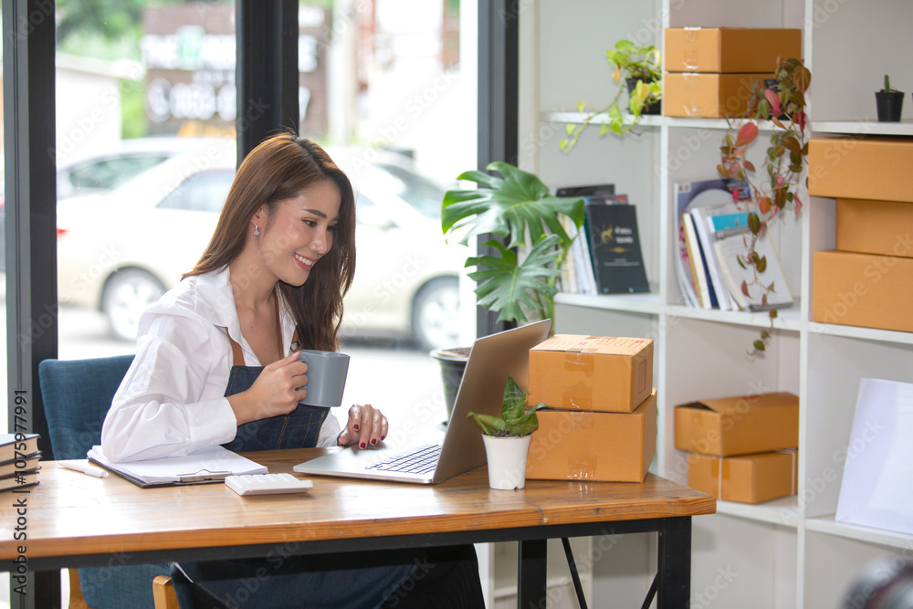 Beautiful business woman Happy working online shopping at her store. Through phone, computer, young woman seller prepares parcel boxes to send to customers. online sales ecommerce