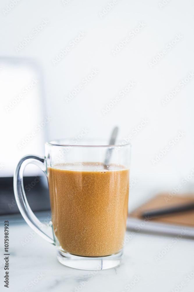 hand holding coffee in clear mug in front of blurred home interior background, habits and lifestyle concept hand holding coffee in clear mug in front of blurred home interior background, habits and lifestyle concept