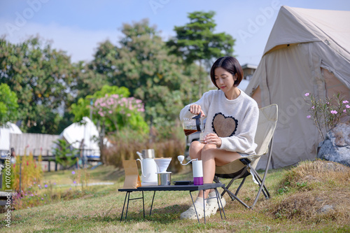 A woman is seen sipping coffee in a comfortable camping environment with a beige tent and simple coffee makers. Perfect for themes related to outdoor living and camping.