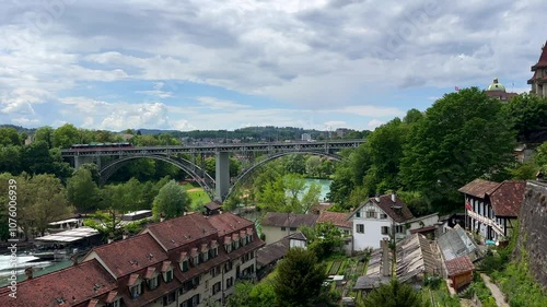 Aerial panning shot of ancient houses with river view and famous bridge of Bern in background. Historic buildings in city capital of Switzerland. Sunny day with clouds in summer. Panorama wide shot.