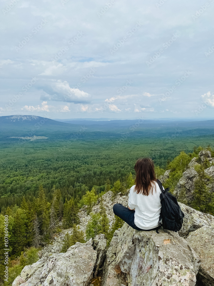 A woman is comfortably sitting on a large rock while she enjoys an amazing view of a vast and beautiful forest stretching far and wide in the distance, surrounded by natures splendor A woman is comfortably sitting on a large rock while she enjoys an amazing view of a vast and beautiful forest stretching far and wide in the distance, surrounded by natures splendor