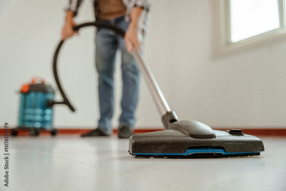 Fototapeta premium A man cleaning a living room with a vacuum cleaner.